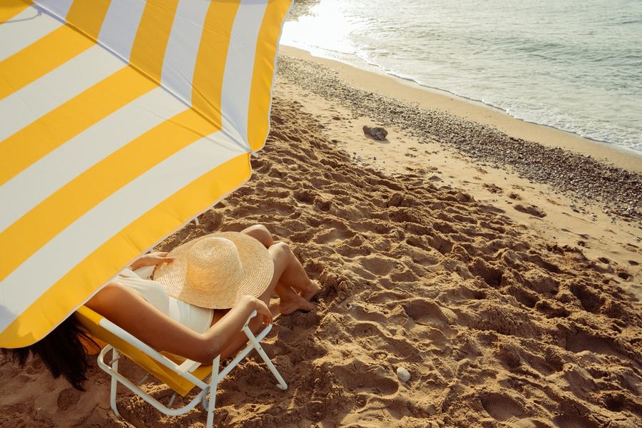 Chaise longue sous un parasol rayé jaune et blanc au bord de la mer